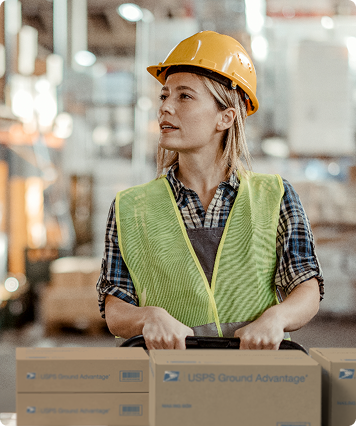 Person pushing a cart full with USPS Ground Advantage shipping boxes on it.